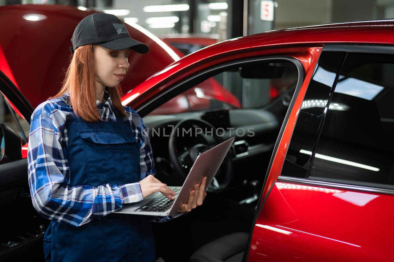 Woman auto mechanic doing diagnostics in car using laptop. by mrwed54