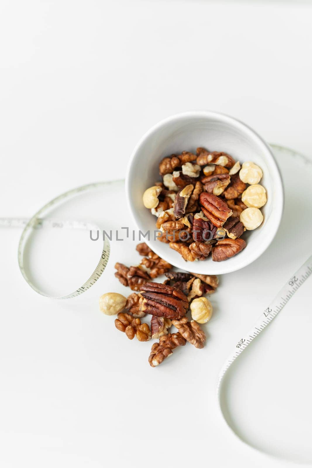 Close-up of a plate with different nuts and a centimeter tape. The concept of weight loss, healthy eating, overweight. Fitness menu. by sfinks