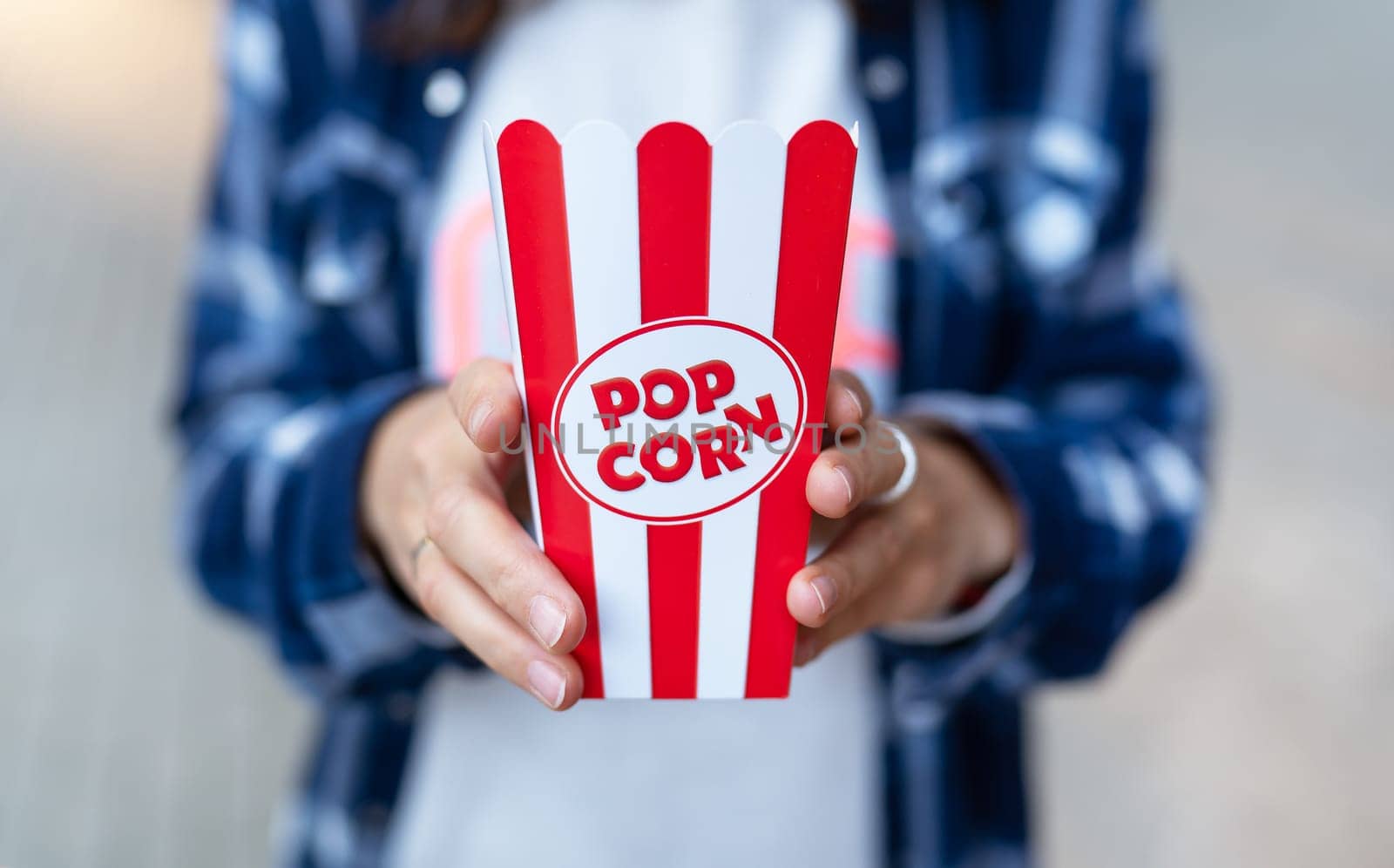 The girl holds in her hands a classic red box of popcorn outdoors. Going to the cinema