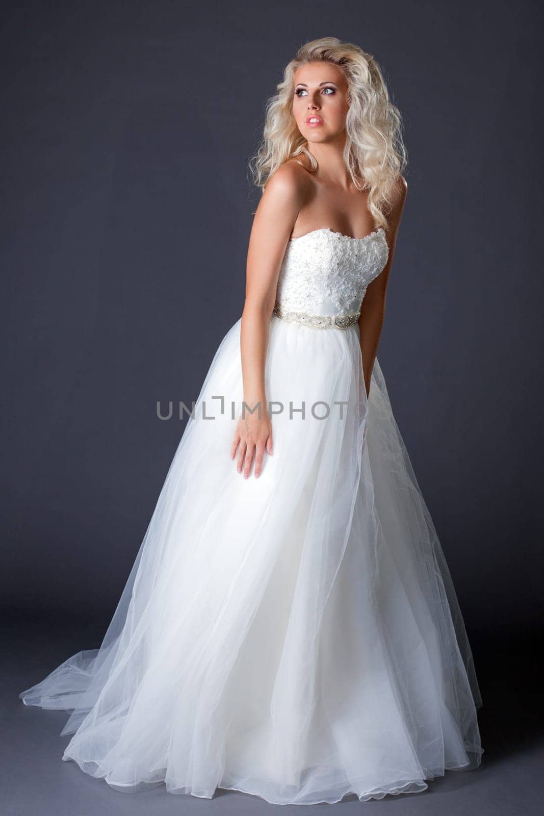 Romantic model posing in fashionable wedding dress, on gray background