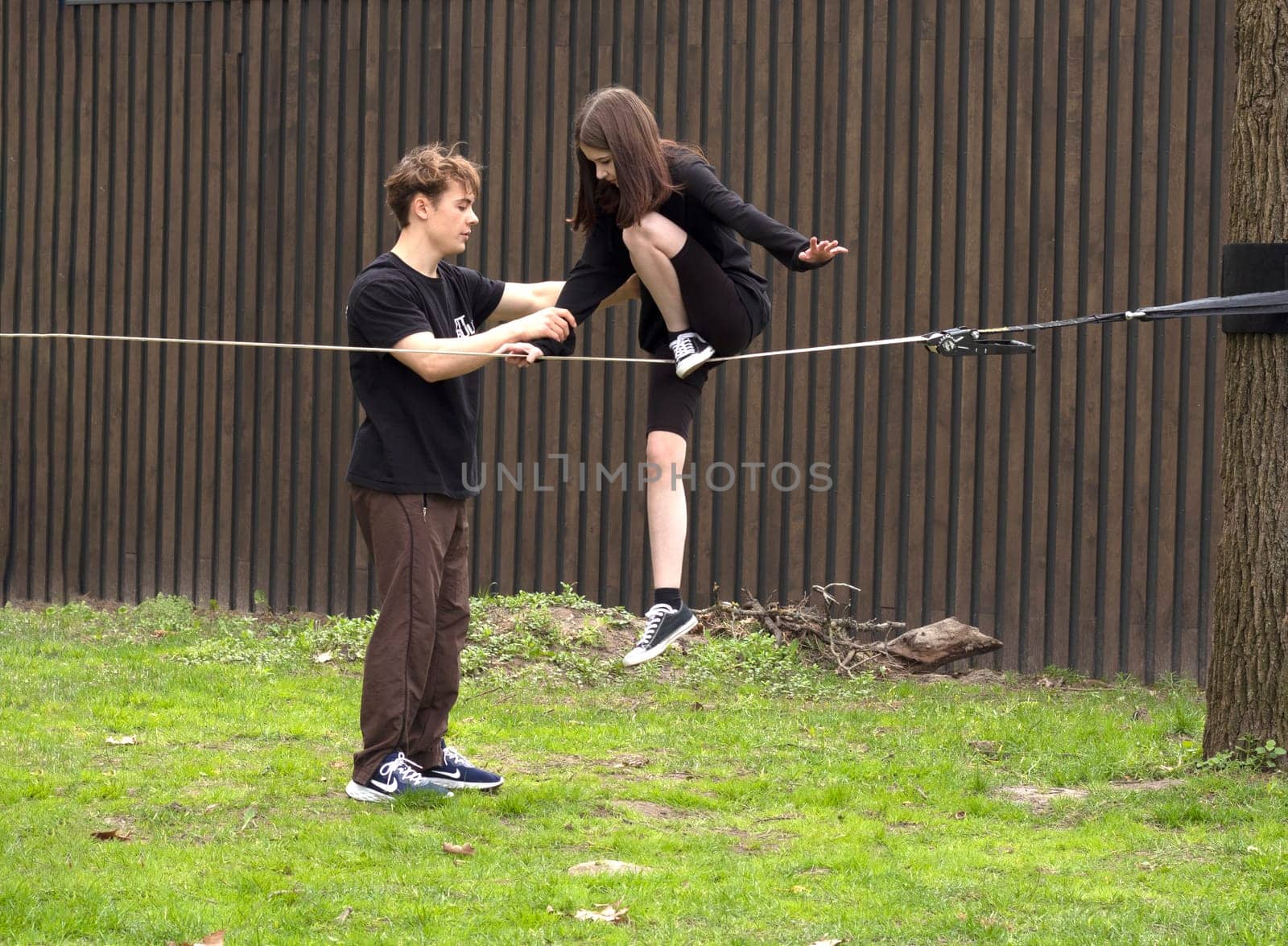 Ukraine. Kyiv, 23.04.2023 guy holds hand his girlfriend. man teaches young woman how walk tightrope. rehearsal. risk challenge concept. woman balancing on slackline rope. active lifestyle, extreme.