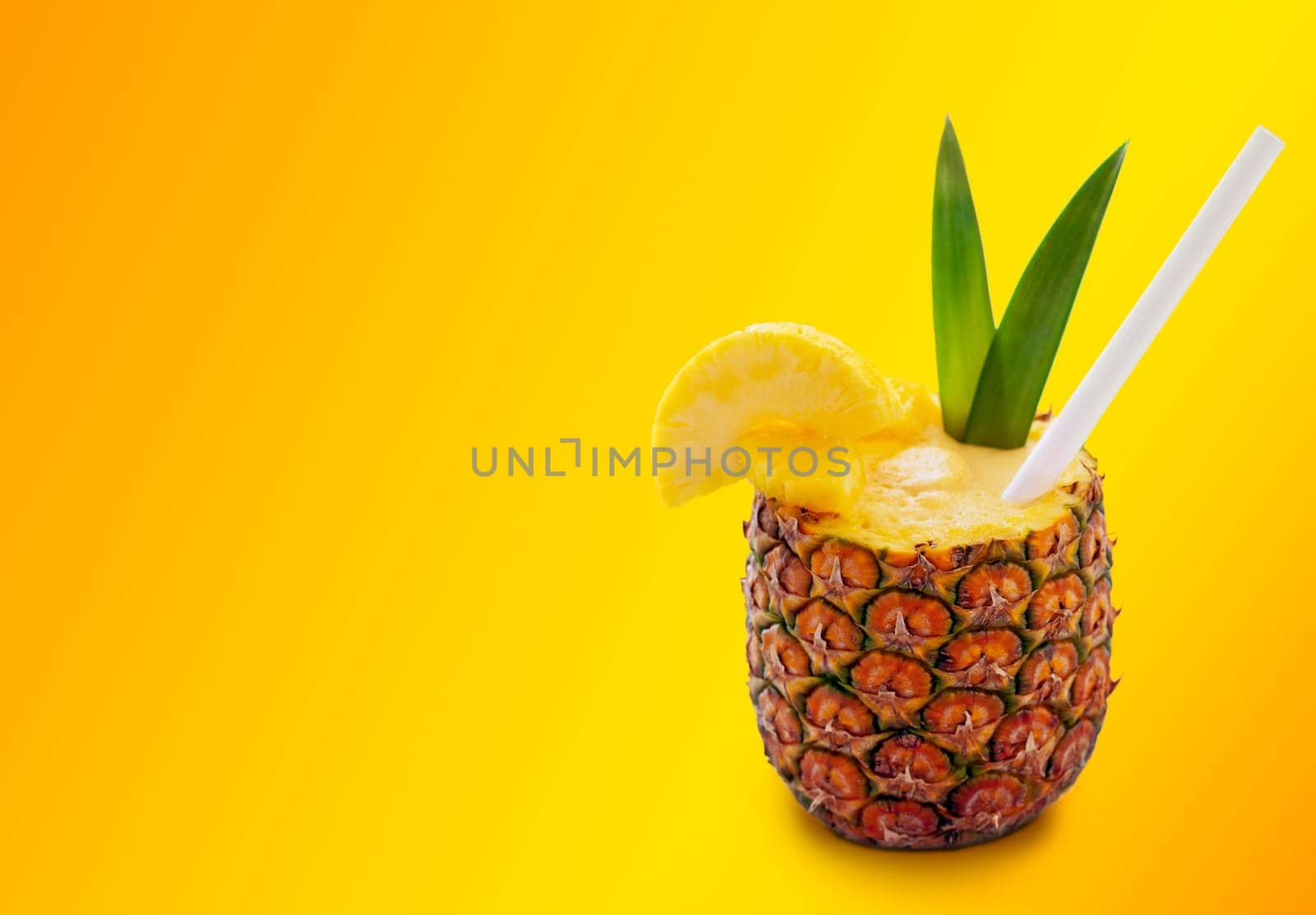 Pina colada cocktail in pineapple with straw, pineapple slices, and two green leaves on the orange background