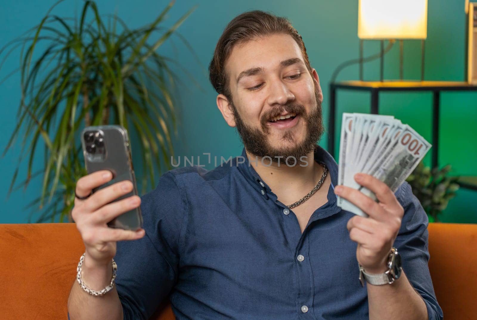 Smiling happy lebanese man counting money cash use smartphone, income saves lottery win budget by efuror