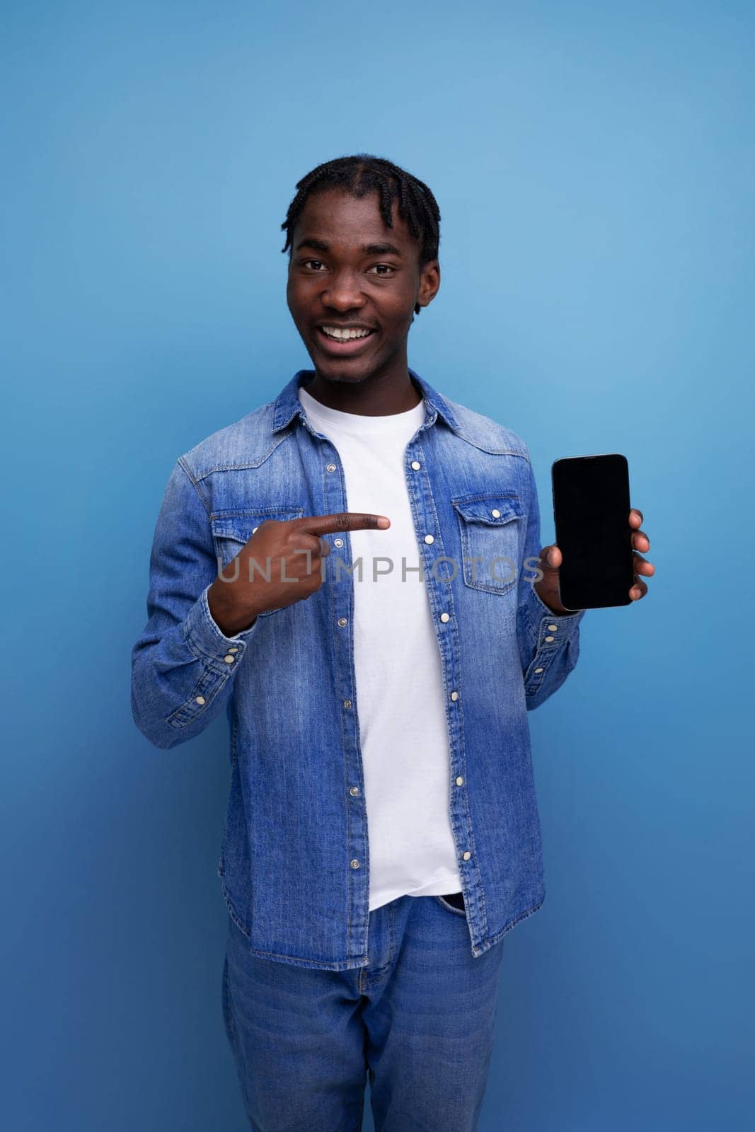 portrait of stylish manager young african man with dreadlocks in denim jacket with smartphone mockup.