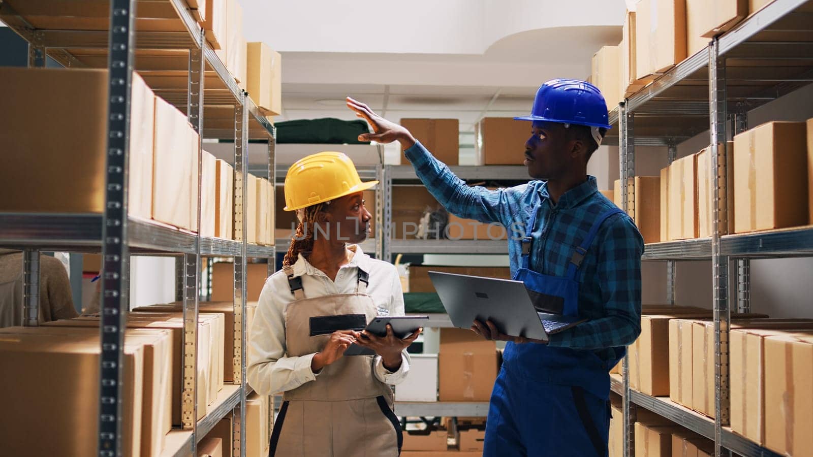 Man and woman organizing products on racks and shelves, looking at merchandise stock on laptop and tablet. Team of workers with overalls arranging goods in storage room, order shipment.