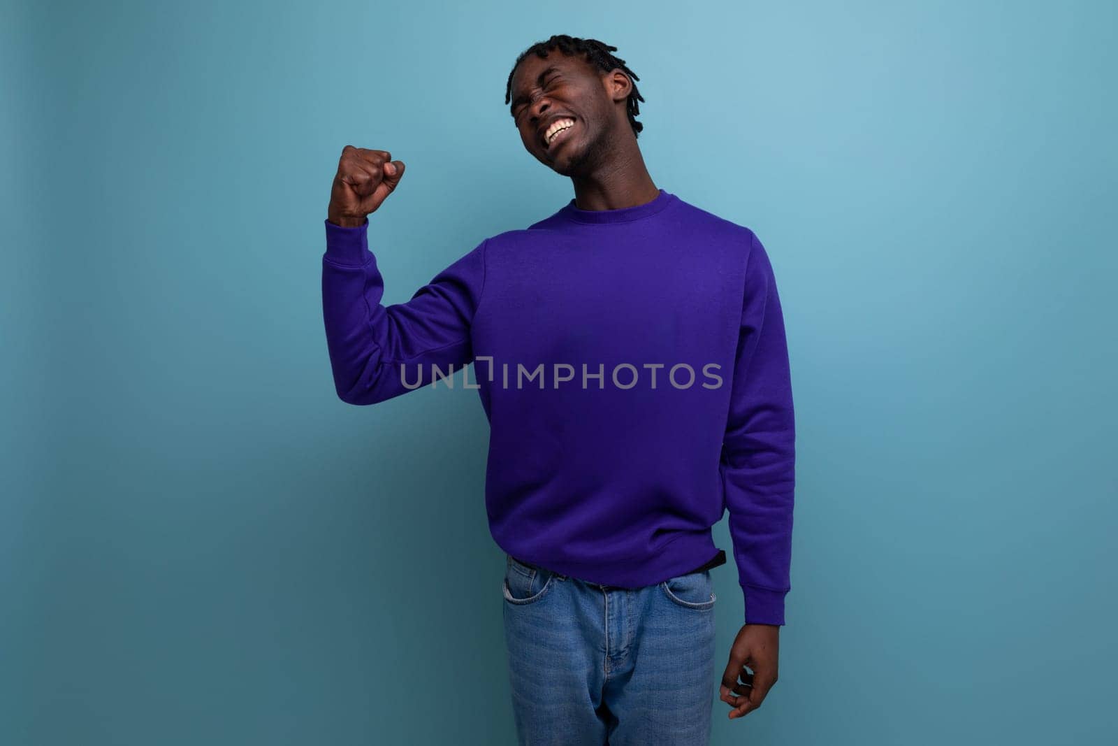 dark-skinned young brunette man with dreadlocks in a blue sweatshirt shows muscles.