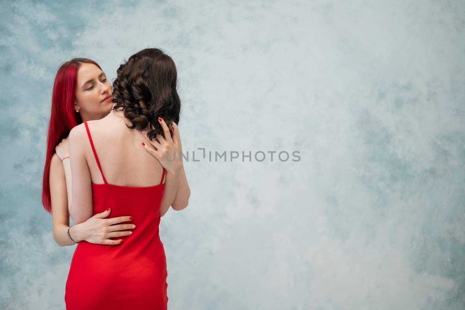 A close-up portrait of two tenderly embracing women dressed in identical red dresses. Lesbian intimacy