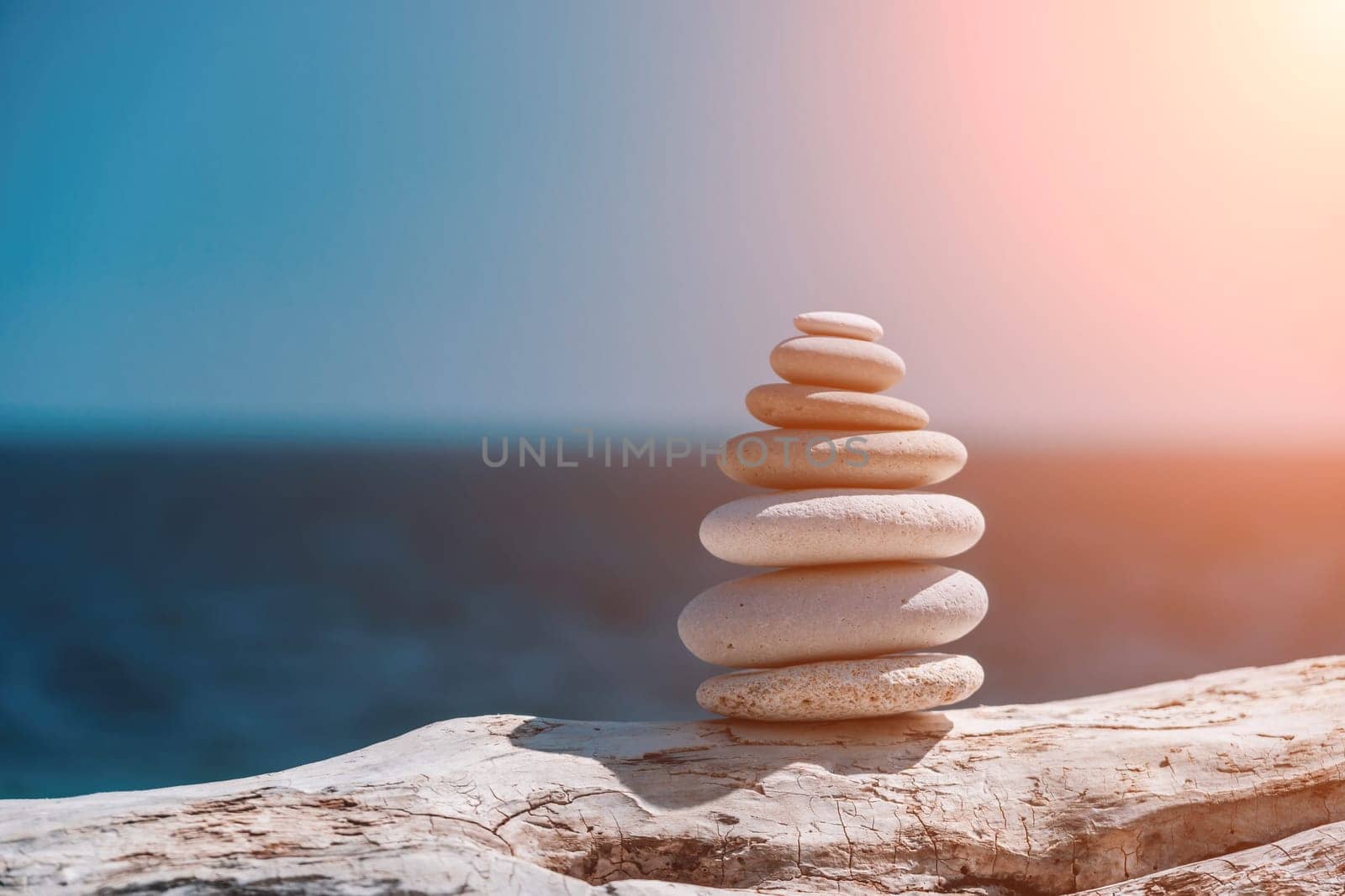 Pyramid stones on the seashore with warm sunset on the sea background. Happy holidays. Pebble beach, calm sea, travel destination. Concept of happy vacation on the sea, meditation, spa, calmness.