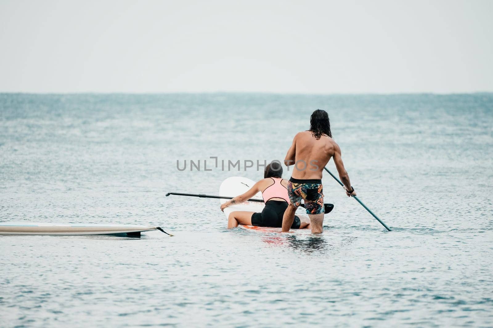 Sea woman and man on sup. Silhouette of happy young woman and man, surfing on SUP board, confident paddling through water surface. Idyllic sunset. Active lifestyle at sea or river