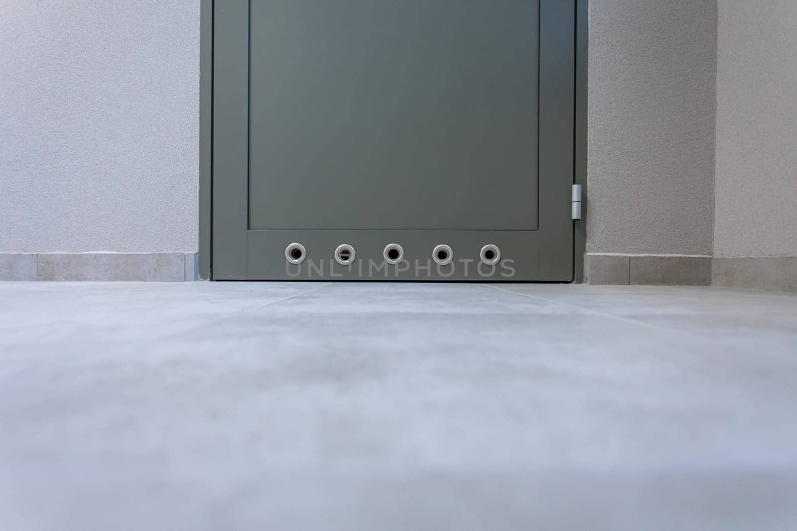 Fragment of the lower part of the aluminum door with holes causing continuous ventilation of wet rooms. View near the floor itself.