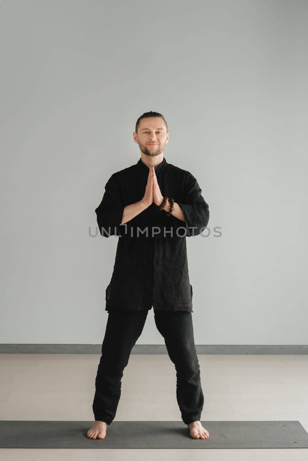 A man in black kimano practicing qigong energy exercises indoors by Lobachad