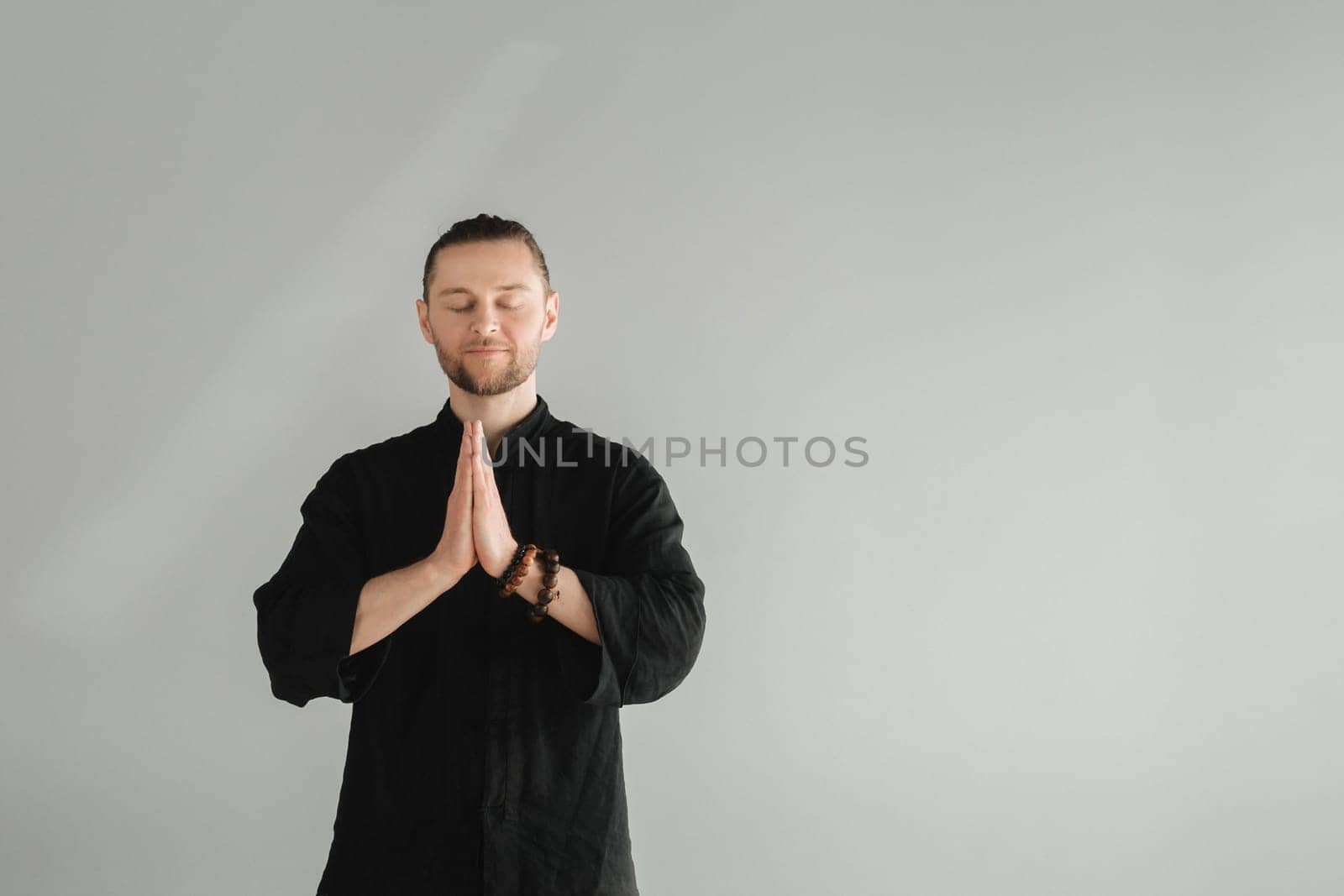 A man in black kimano practicing qigong energy exercises indoors.