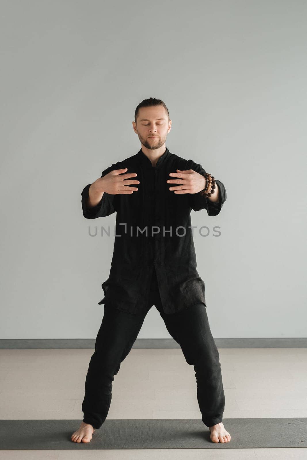 A man in black kimano practicing qigong energy exercises indoors.