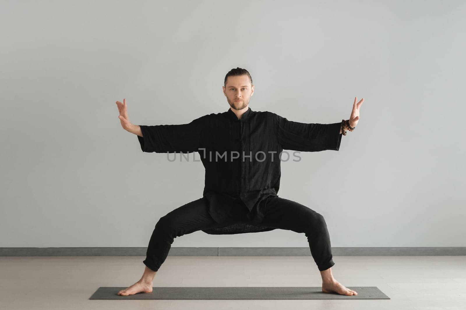 A man in black kimano practicing qigong energy exercises indoors.