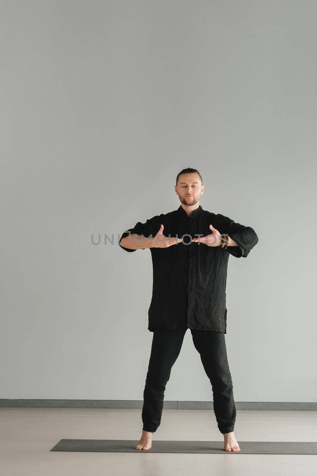 A man in black kimano practicing qigong energy exercises indoors.