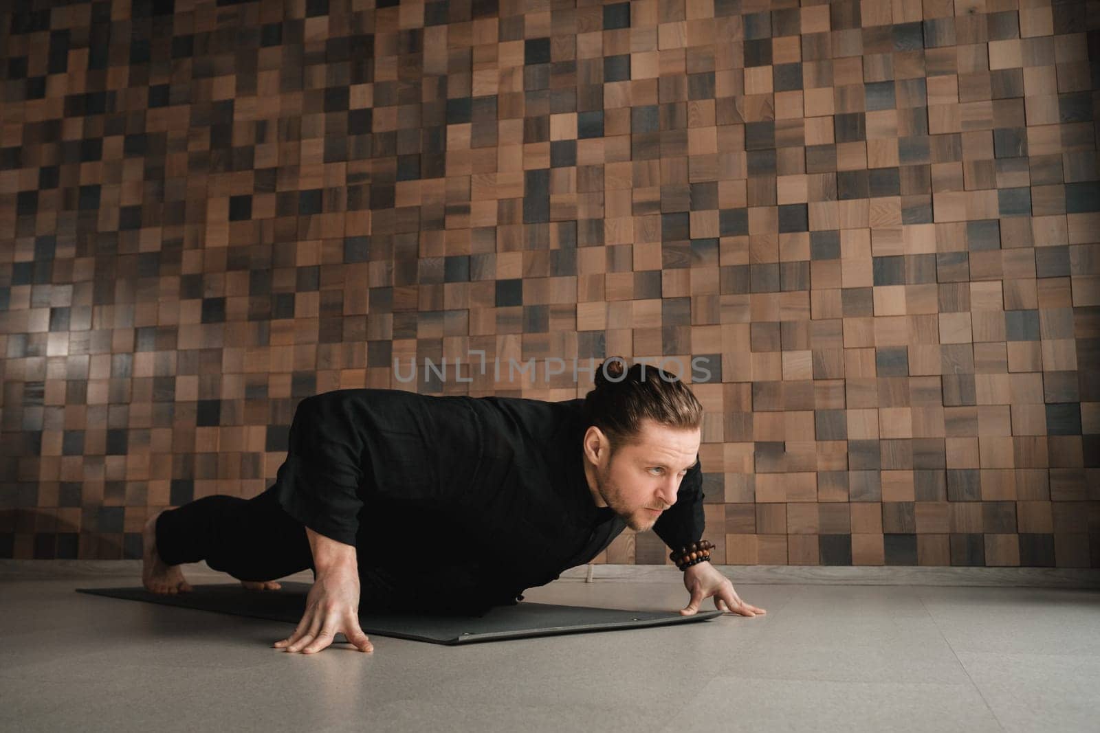 A man in black kimano practicing qigong energy exercises indoors.