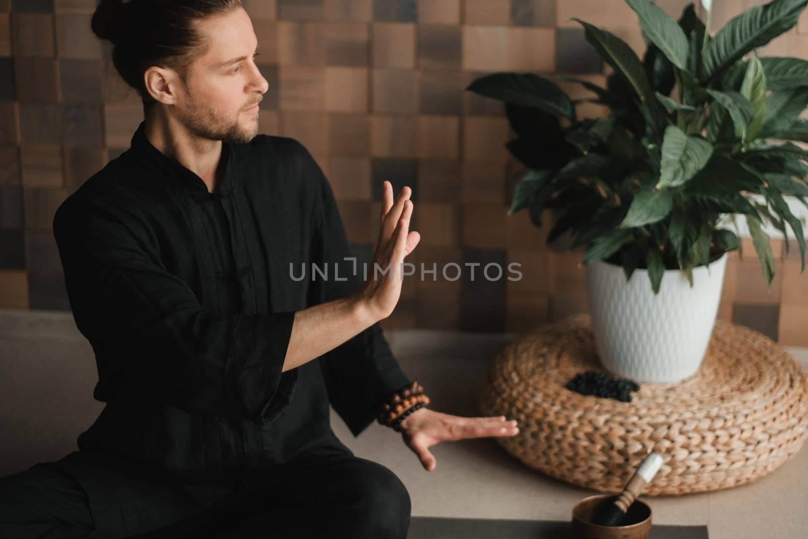 Portrait of a young man in a black kimano sitting in a lotus position on a gym mat in the interior by Lobachad