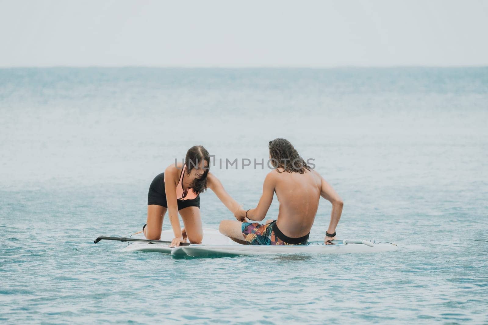 Sea woman and man on sup. Silhouette of happy young woman and man, surfing on SUP board, confident paddling through water surface. Idyllic sunset. Active lifestyle at sea or river