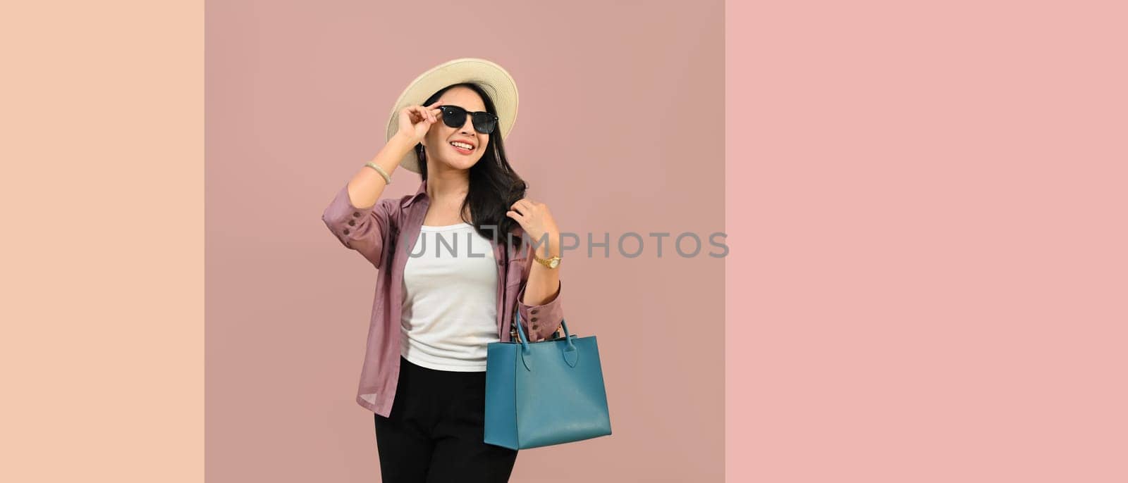 Portrait of cheerful young woman wearing summer clothes and sunglasses isolated on pink background with copy space.
