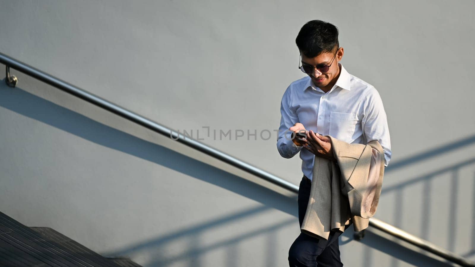 Millennial businessman using smartphone while sitting outside office building. Modern lifestyle and technology concept by prathanchorruangsak