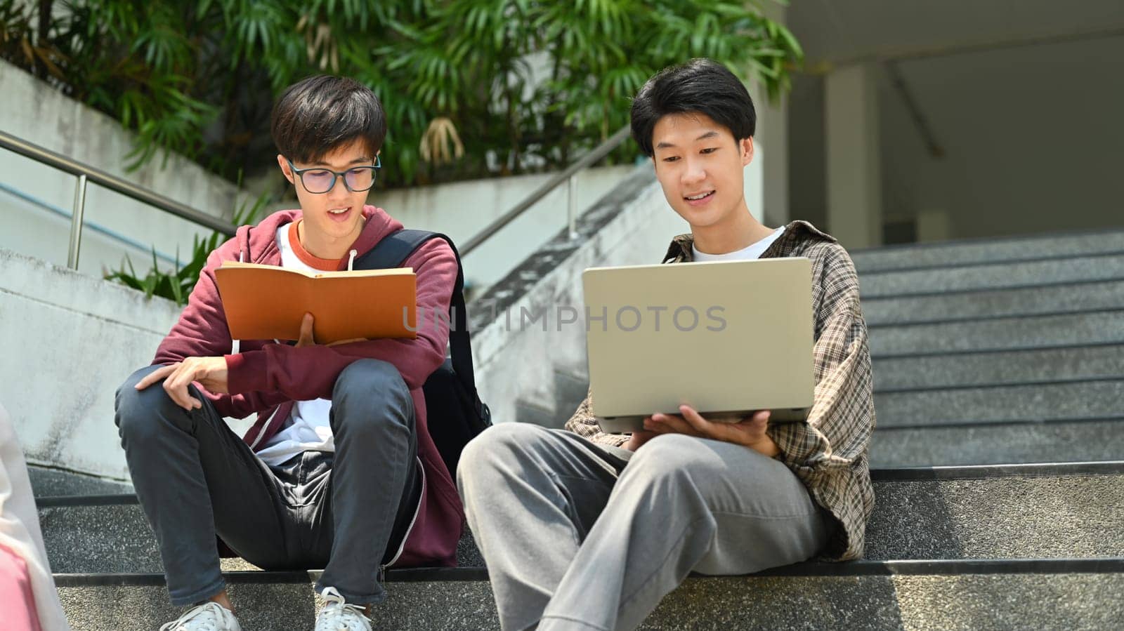 University students sitting on stairs and talking to each other after classes. Education and youth lifestyle concept.