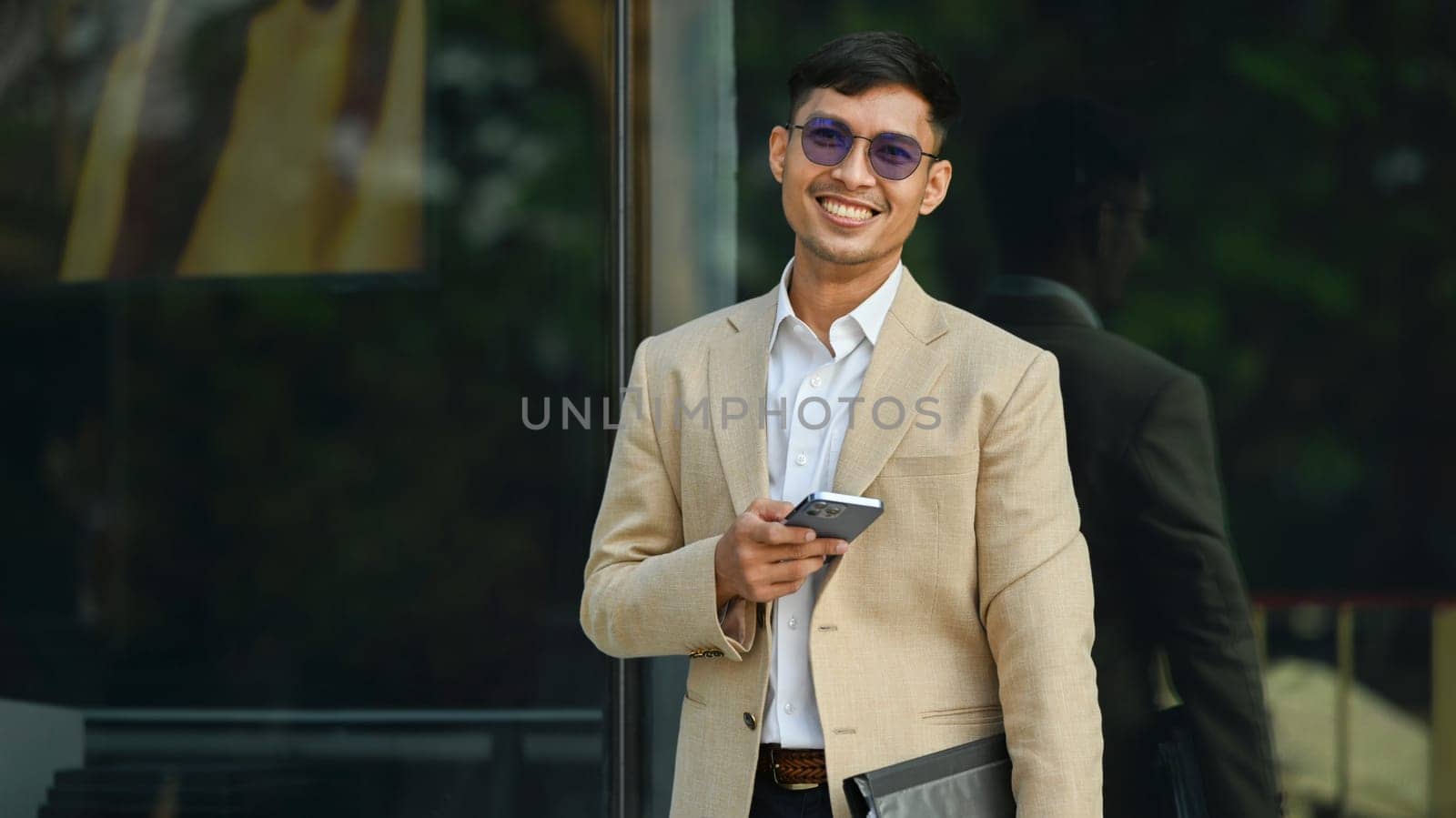 Millennial businessman using smartphone while sitting outside office building. Modern lifestyle and technology concept.