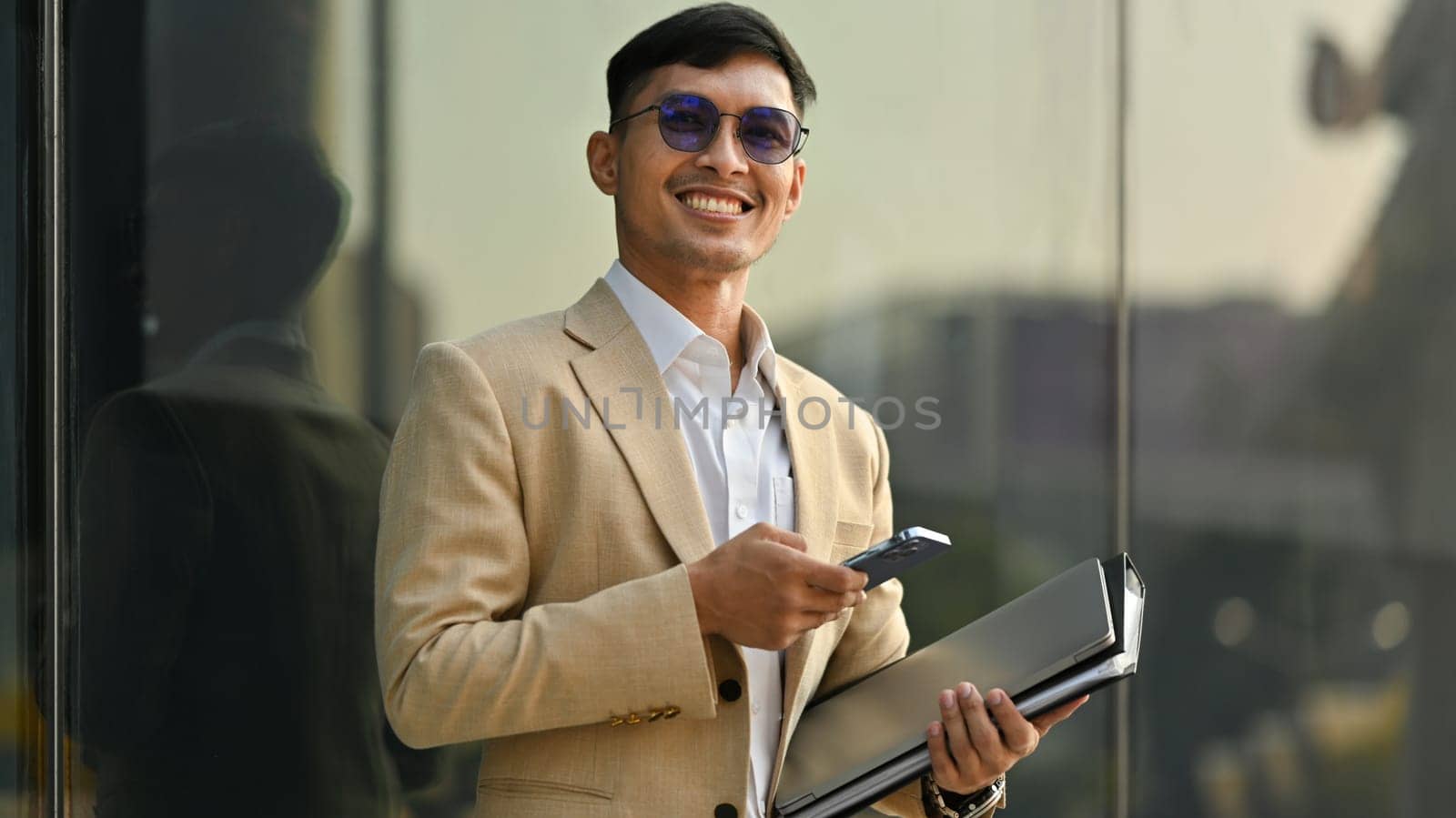 Confident young businessman in elegant suit using smartphone at outdoor. Technology, people and city life concept.
