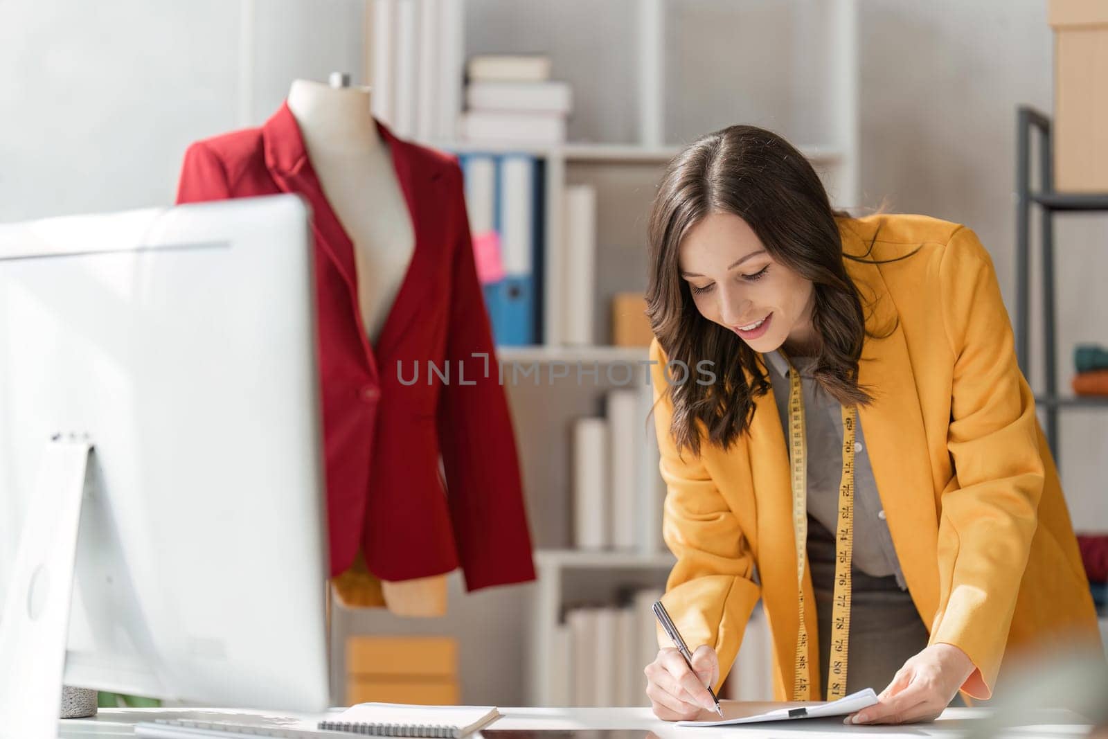 Young attractive female fashion designer sketching idea on paper at desk, working with a laptop at home.