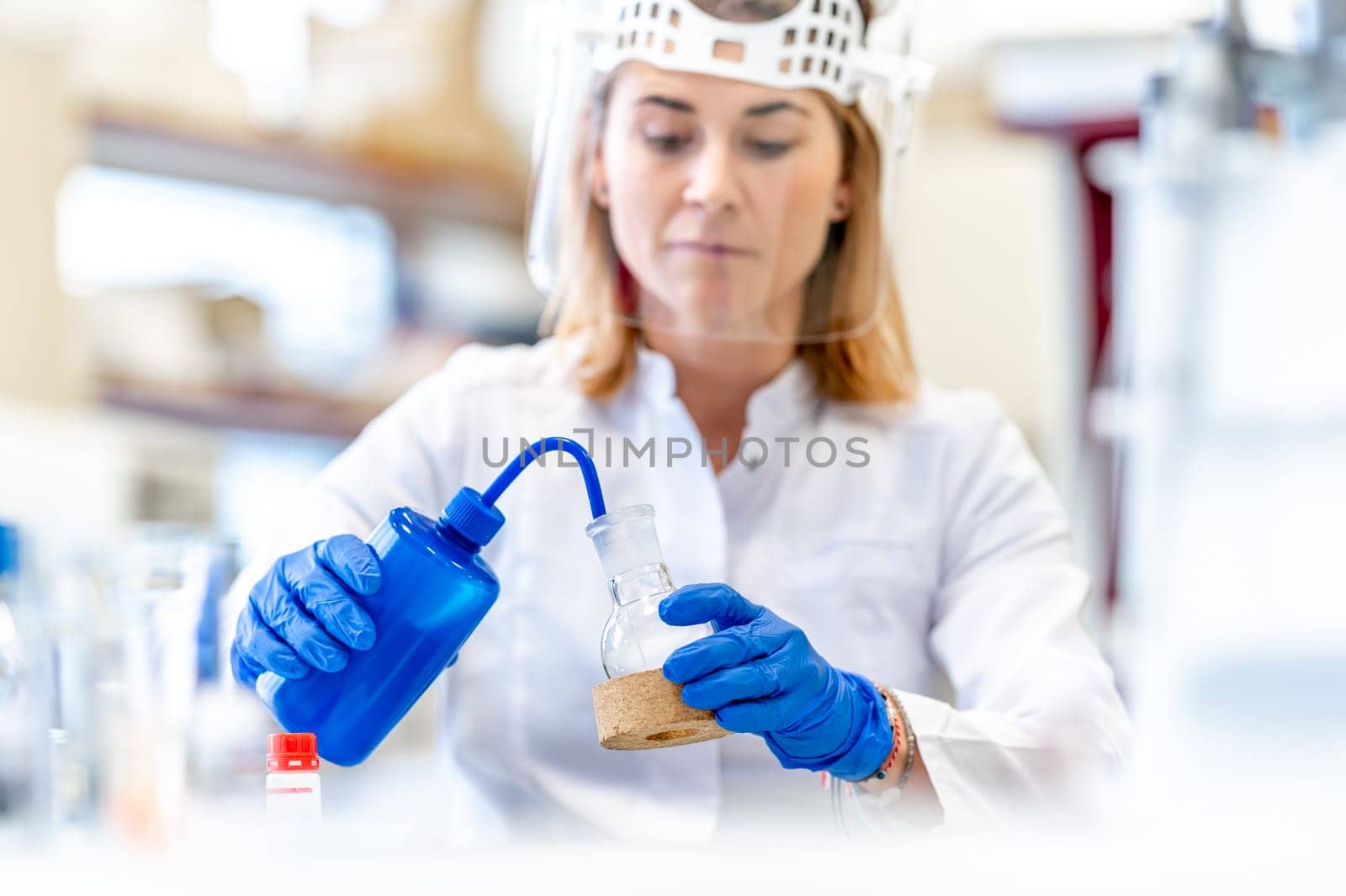 a woman conducts research on dangerous chemical substances in the biochemical laboratory of the Scientific Institute. Use protective equipment, glass face mask and rubber gloves by Edophoto