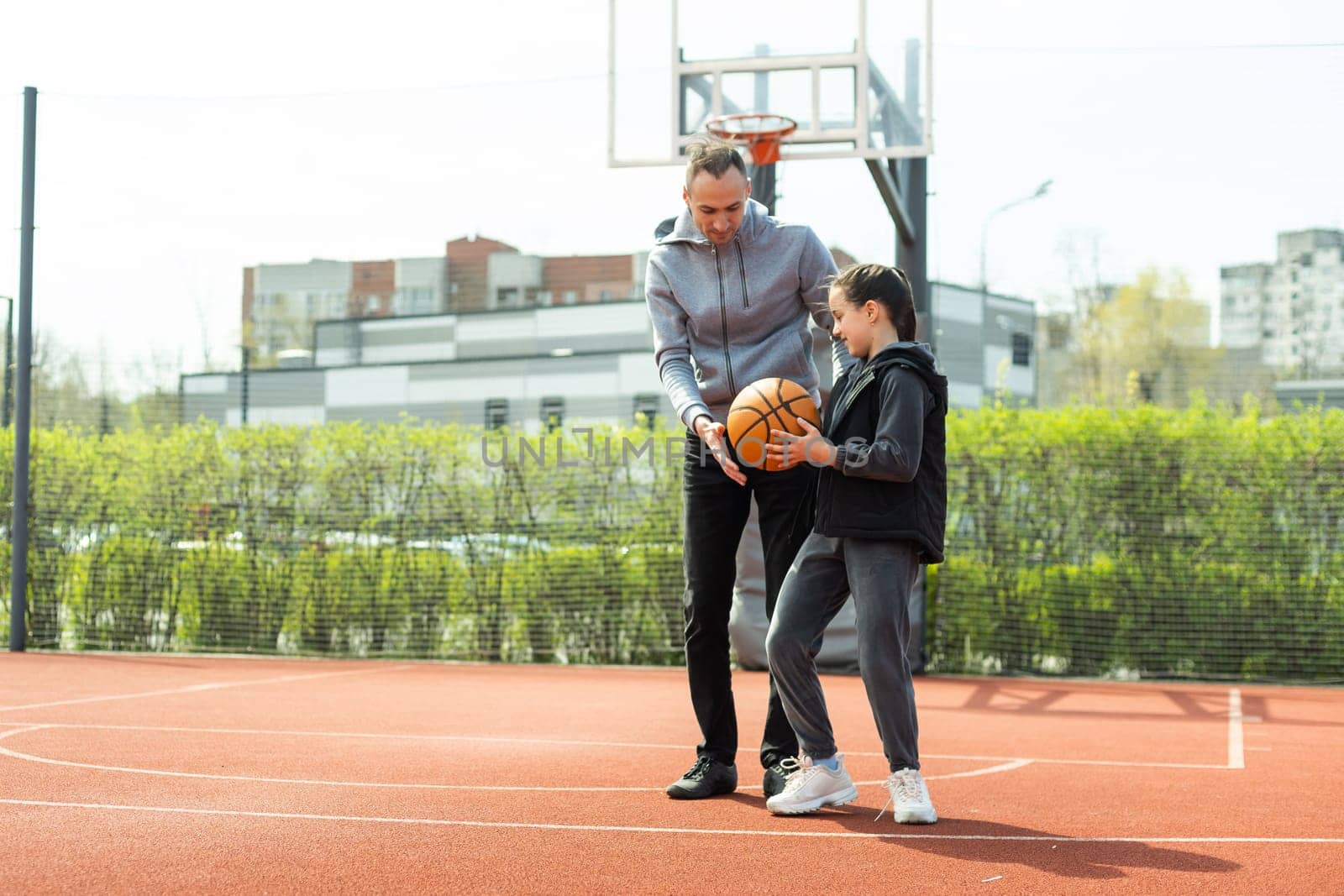 Father and teenage daughter playing basketball outside at court by Andelov13