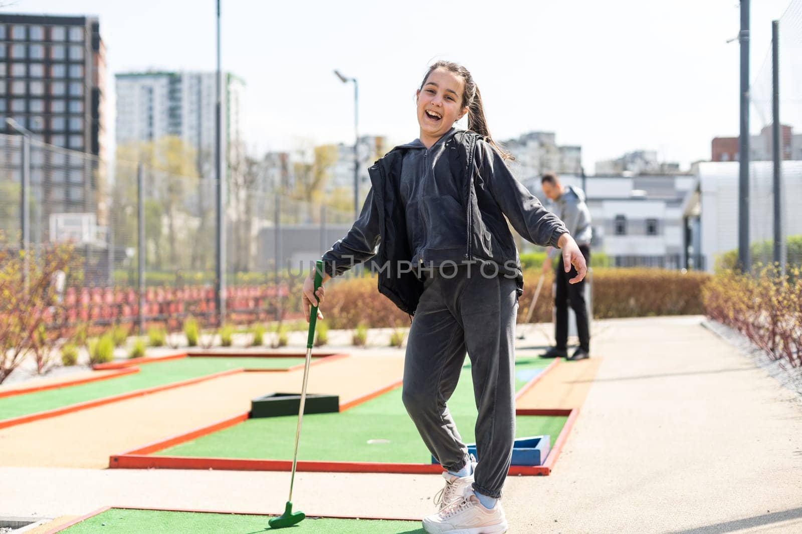Beautiful toddler european model child girl posing with mini golf equipment on green field outdoor in tropical resort