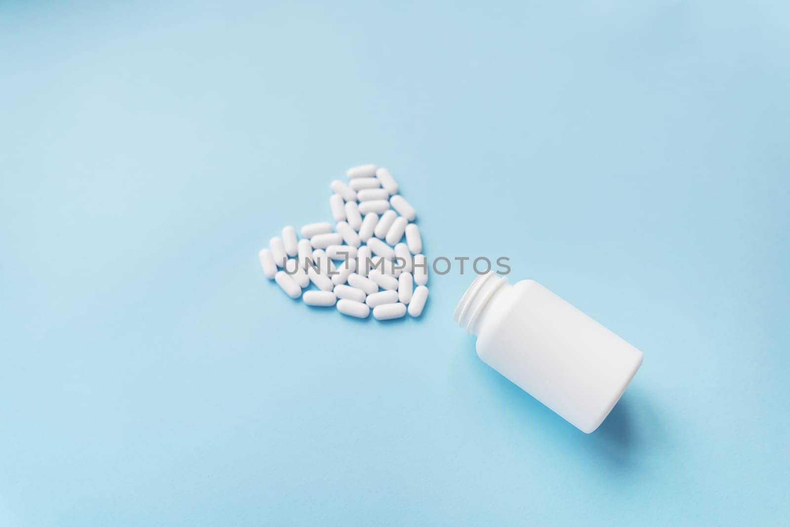 White pills in the shape of a heart came out of a jar on a blue background, health and heart problems together with a plastic jar. The concept of medicine and health care