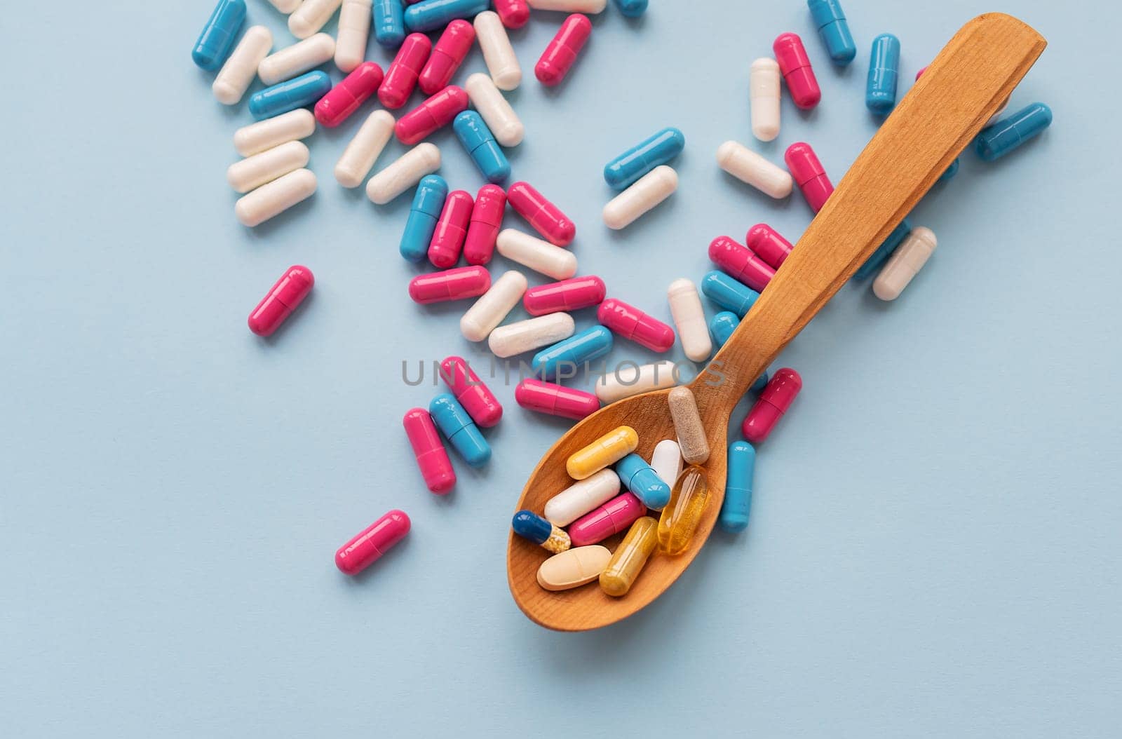 Various bright pills on a blue background lie in a wooden spoon against the background of different bright pills. Health care concept