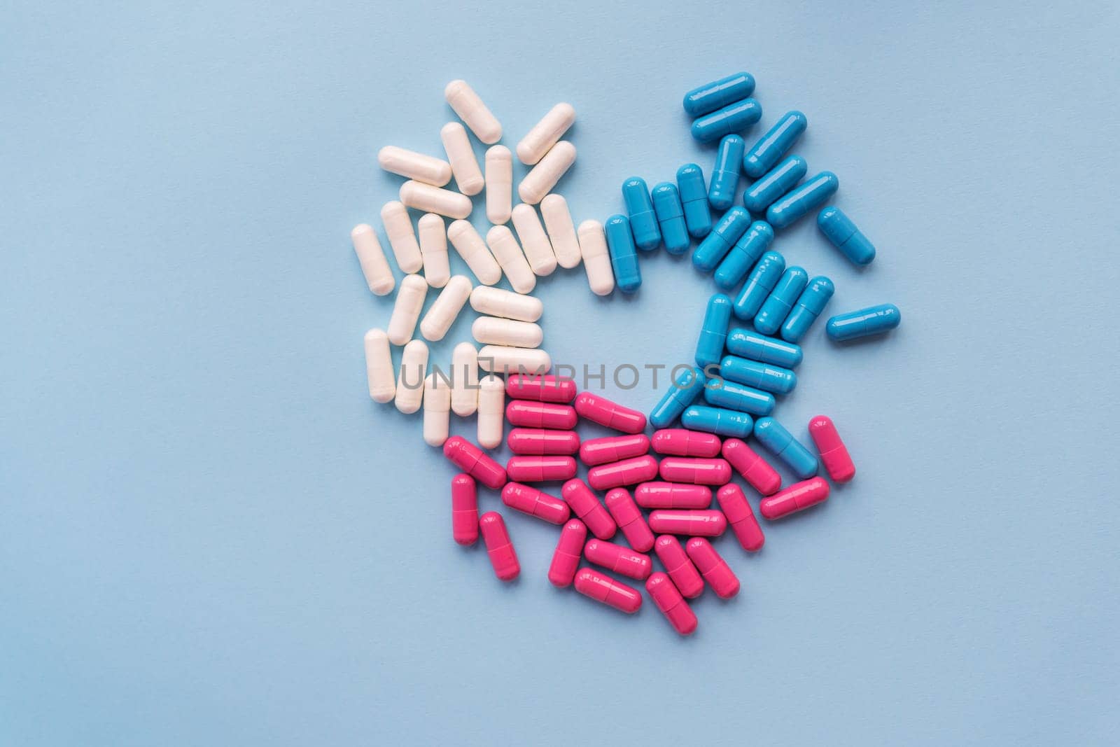 Various colored pills - blue, pink, white laid out in the shape of a heart, isolated on a blue background. Place for inscription