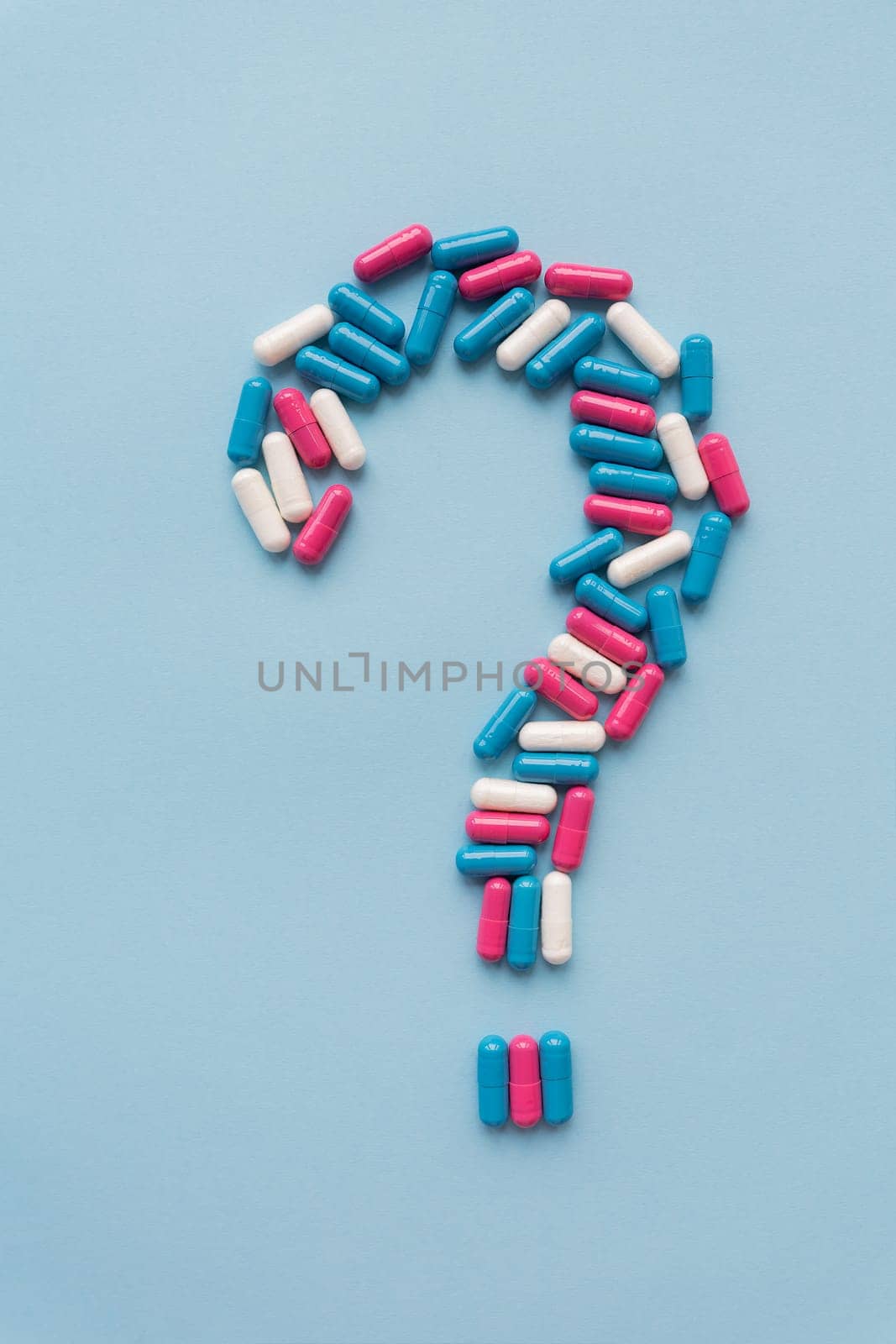 Question mark consisting of three multi-colored vitamins on a blue background. Health problems and treatment. The concept of evidence-based medicine. by sfinks