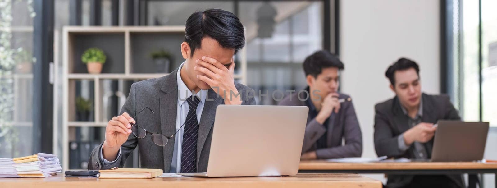 Focused serious professional using laptop in office lobby. Young asian man using laptop in background. Wireless technology concept..