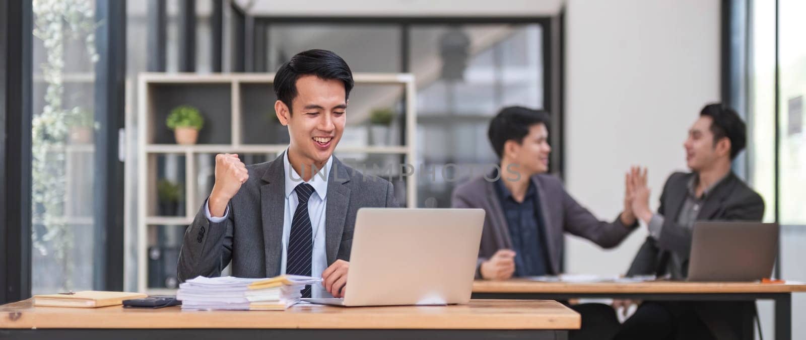 Portrait of confident young businessman using laptop while colleague in background by wichayada