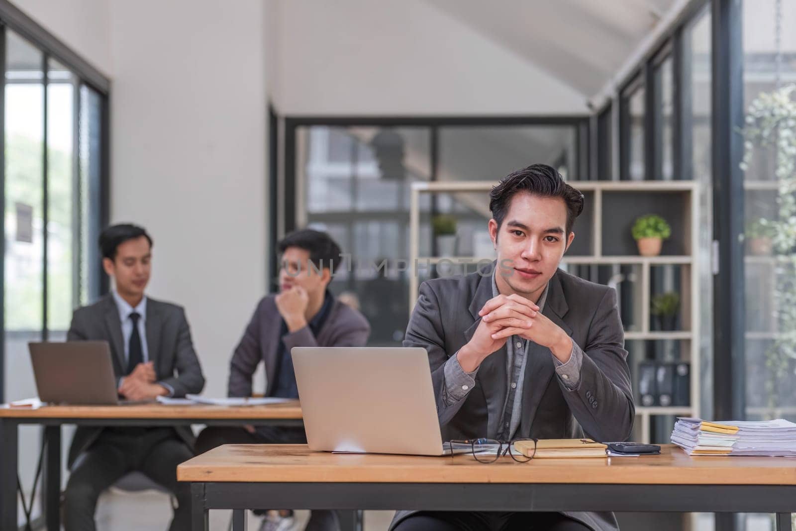 Portrait of confident young businessman using laptop while colleague in background by wichayada