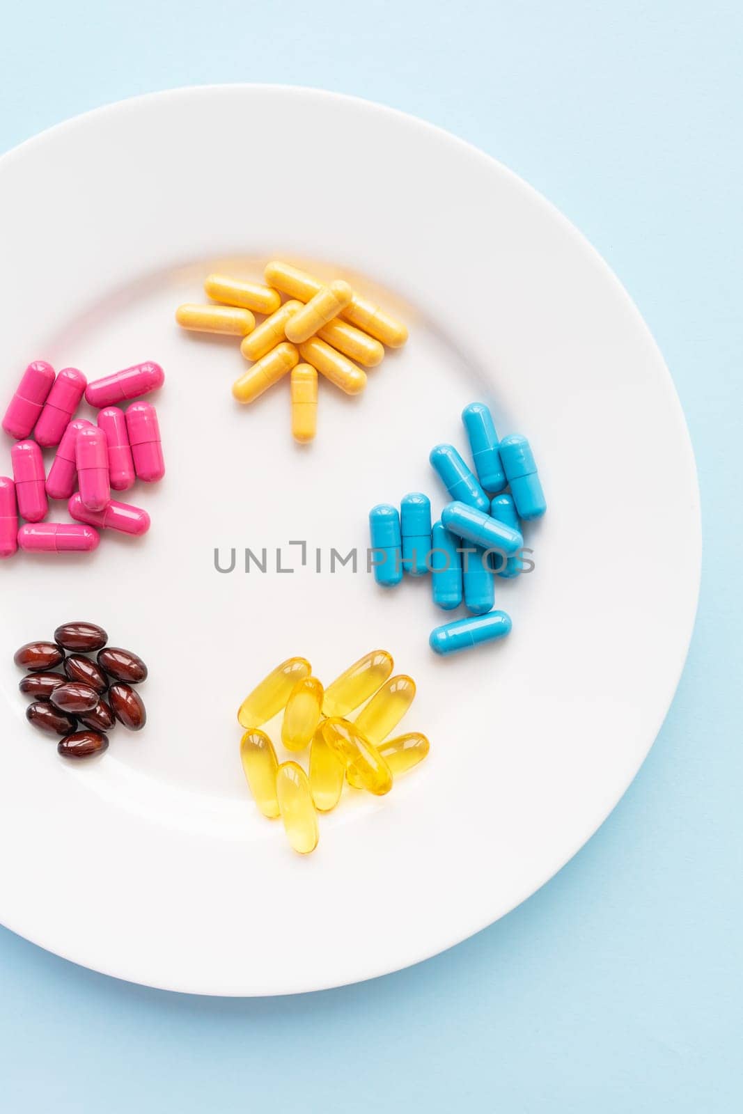 Food supplements of bright color lie on a white plate on a blue background. Concept of health support and lack of vitamins. Vertical photo, close-up, top view