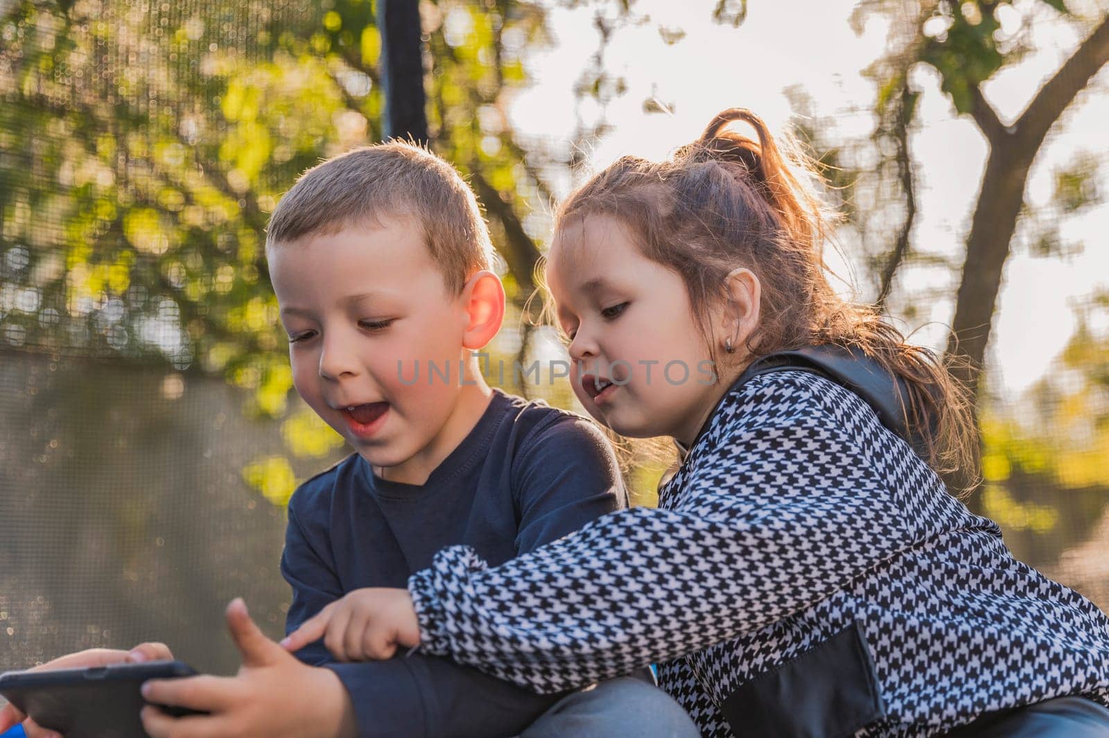 portrait of children who sit on a trampoline and look at the phone