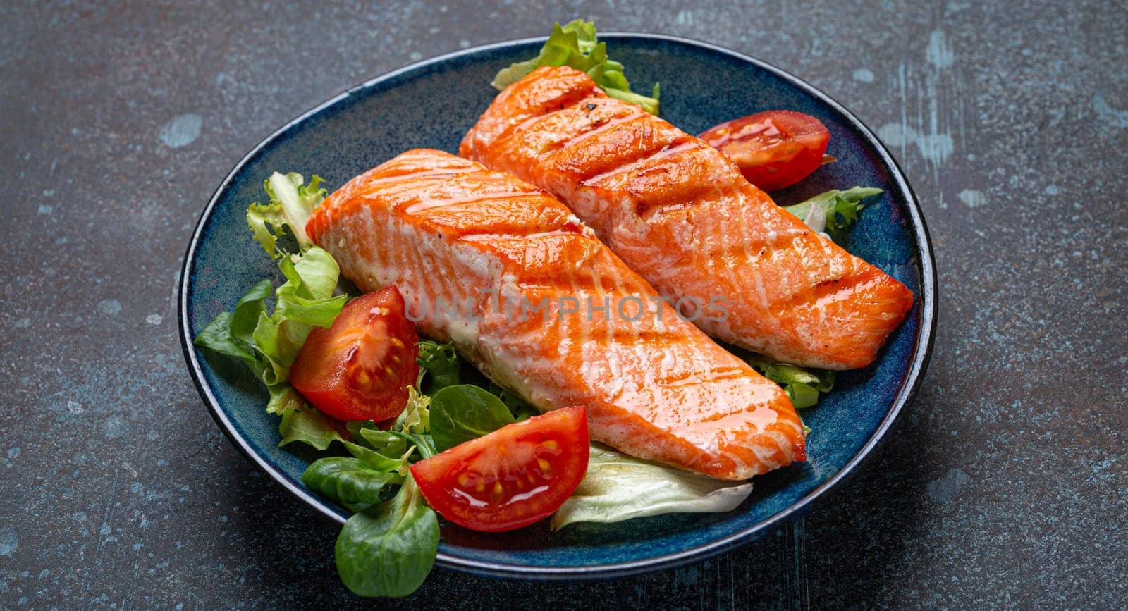 Grilled fish salmon steak with vegetables salad on ceramic plate on rustic stone background angle view, balanced diet or healthy nutrition salad meal with salmon and veggies