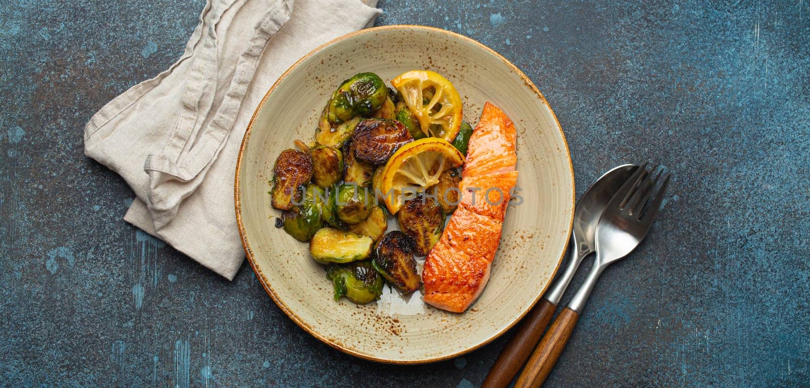 Delicious salmon fillet with grilled Brussels sprouts on plate, rustic concrete background top view. Healthy dinner with grilled fish and vegetables, balanced nutrition by its_al_dente
