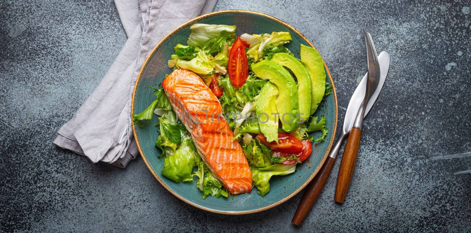 Grilled fish salmon steak and vegetables salad with avocado on ceramic plate on rustic stone background top view, balanced diet or healthy nutrition salad meal with salmon and veggies