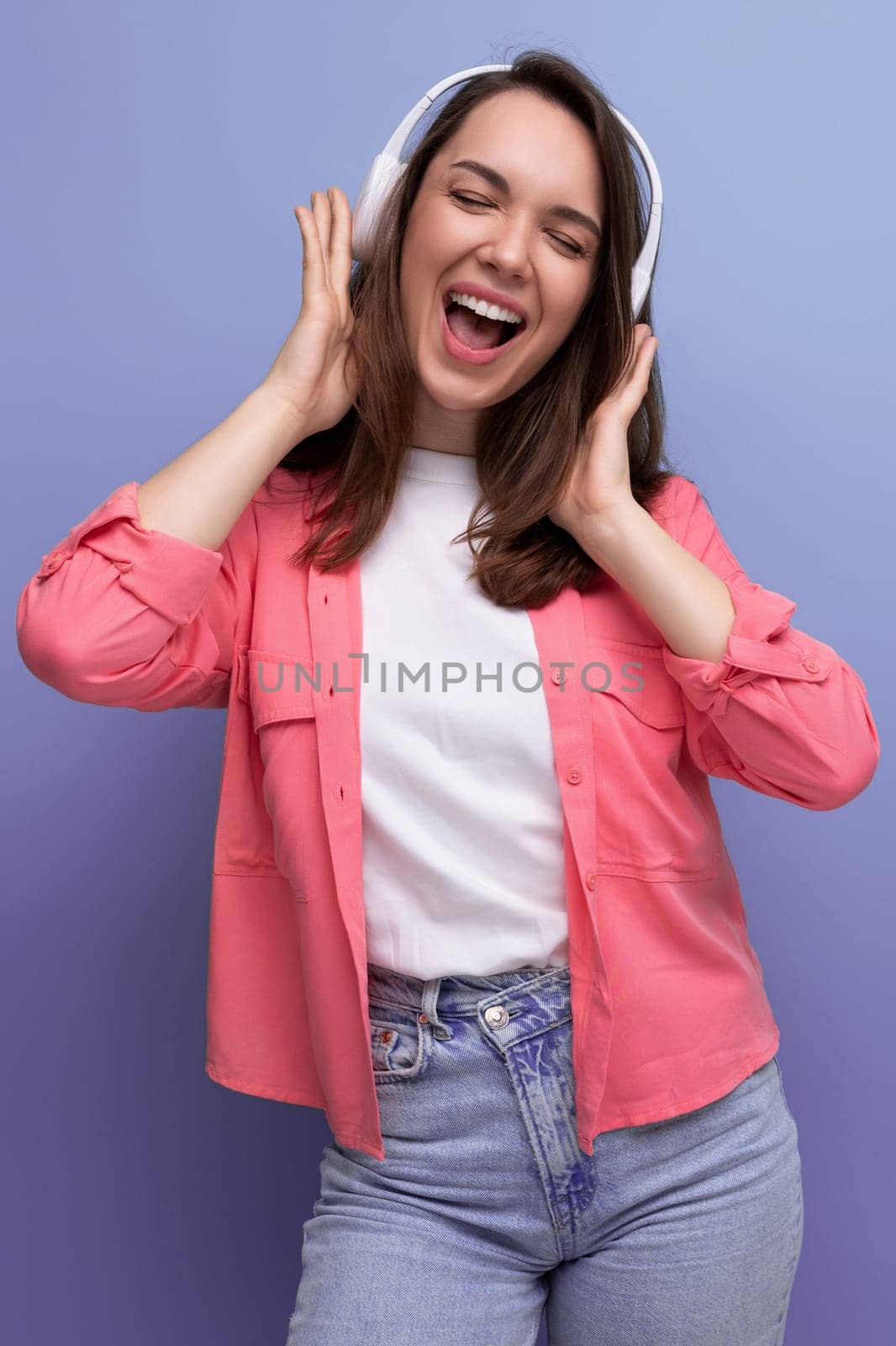 energetic brunette young woman in a shirt and jeans dances to the music from wireless headphones.