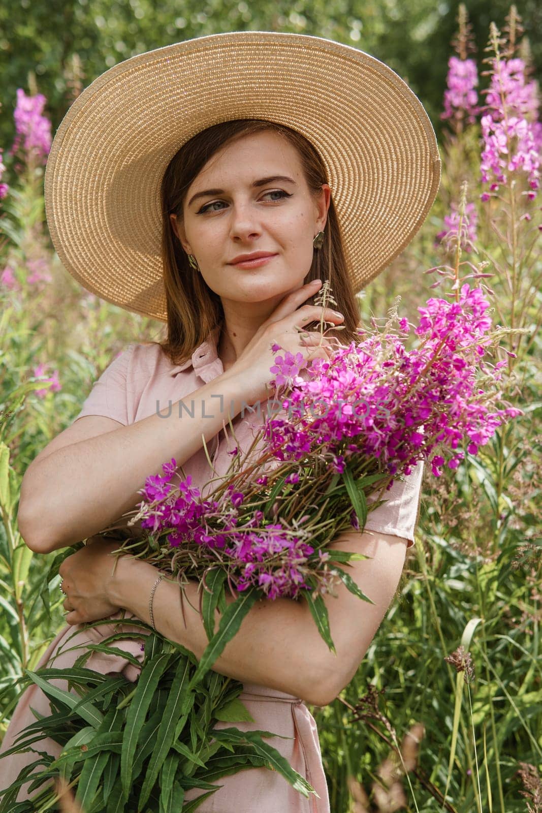 A young woman in nature with a bouquet of pink wild flowers. A bouquet of Ivan-tea in the hands of a woman.