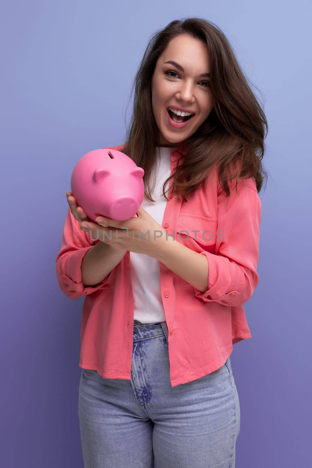 cute brunette young woman in a shirt and jeans saves money for business in a piggy bank by TRMK