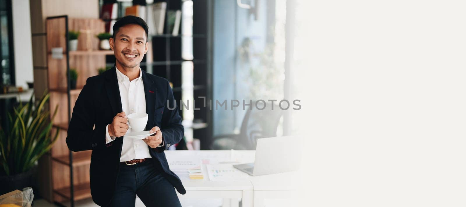 Portrait of an Asian male business owner standing with a computer showing happiness after a successful investment by Manastrong