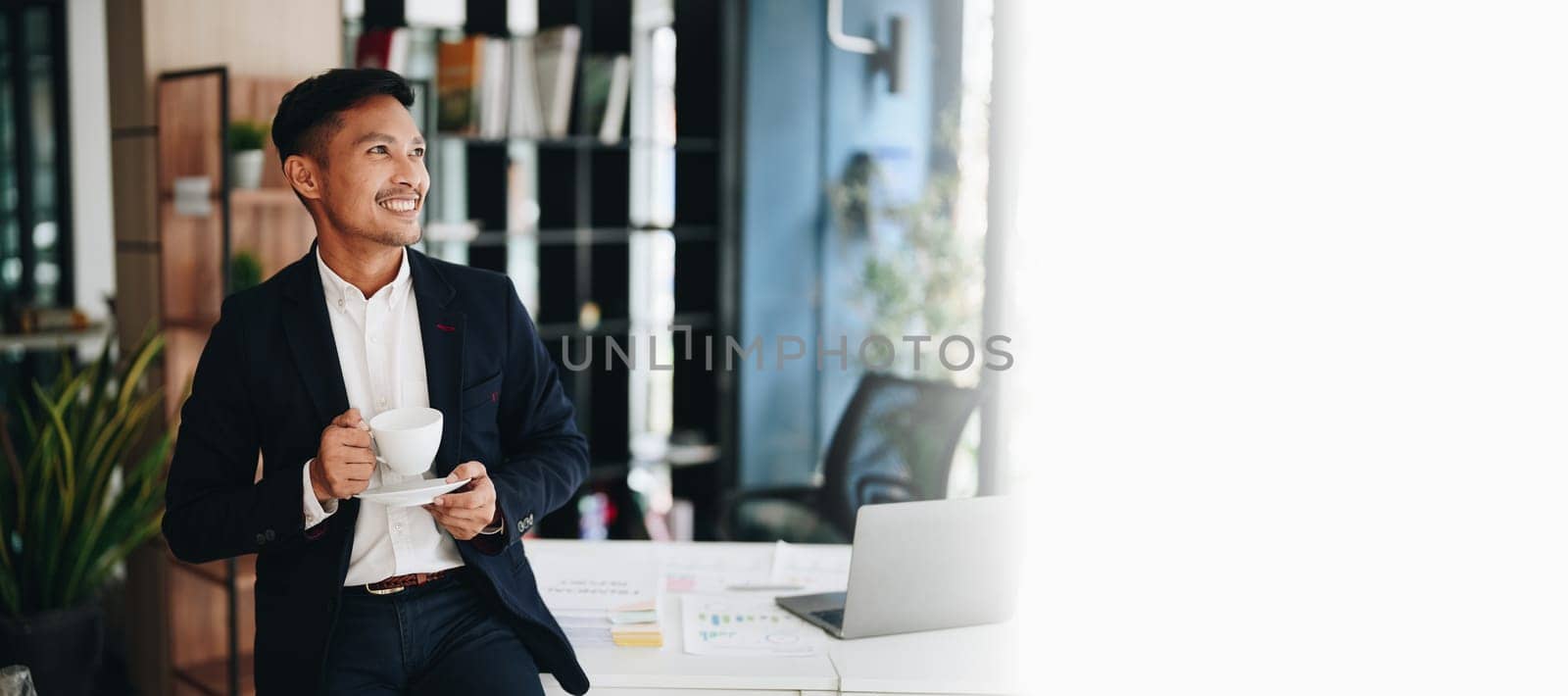 Portrait of an Asian male business owner standing with a computer showing happiness after a successful investment.