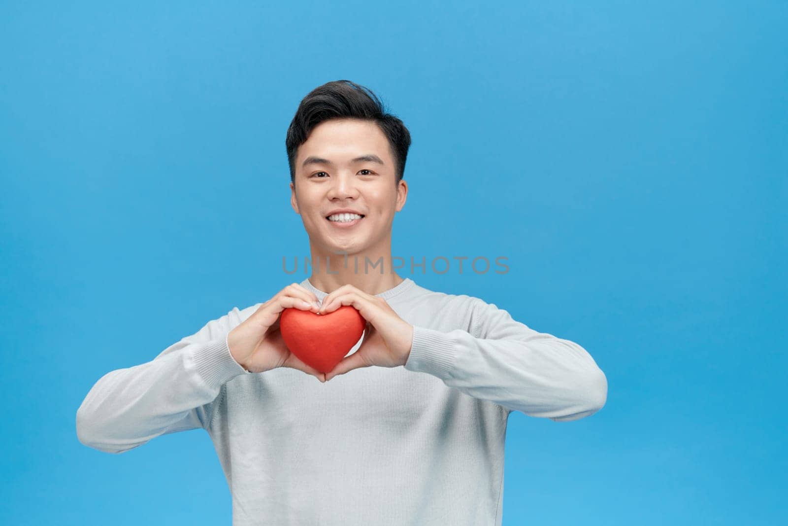 Young man holding red heart over blue background by makidotvn