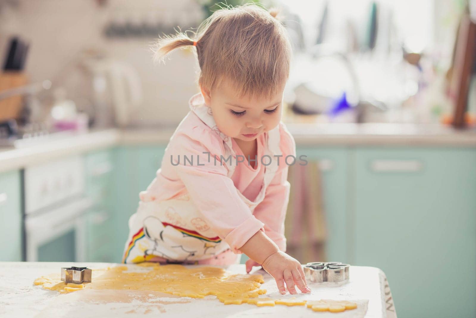 Adorable baby in an apron makes cookies from dough in the kitchen.